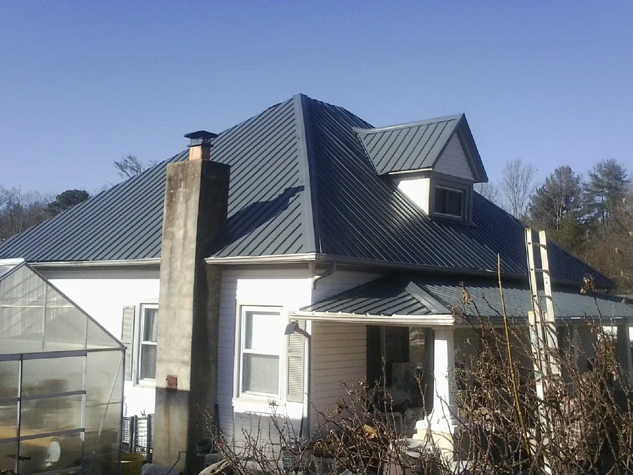 Dark blue standing seam metal roof on a white farmhouse with dormer — Slate & Tile Roof Repair by Roofing Brothers in Guy
