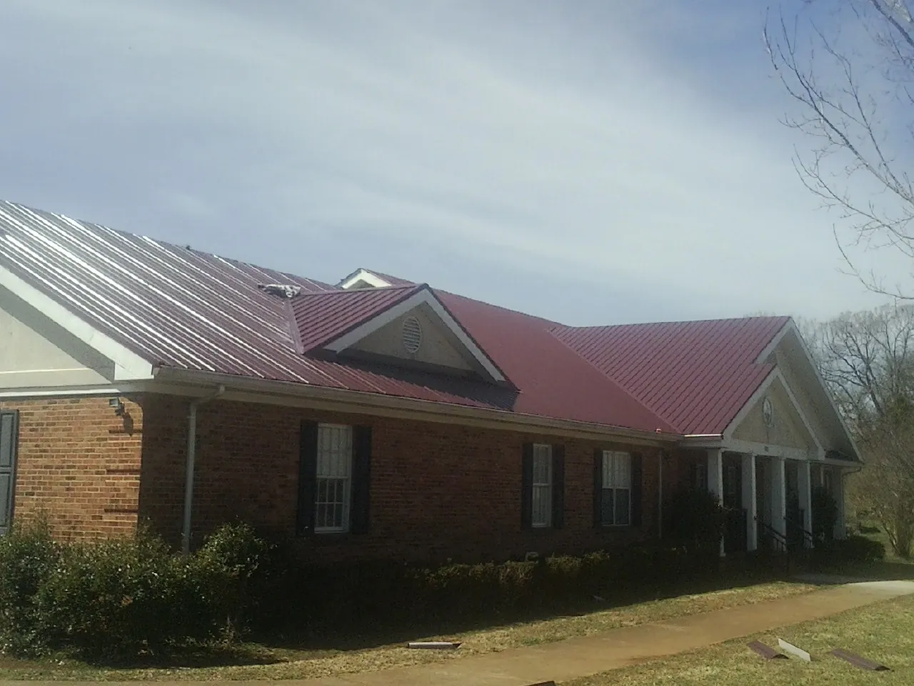 Red metal roof with gabled entries on a long brick building, from a Hail Damage Roof Repair job in Guy