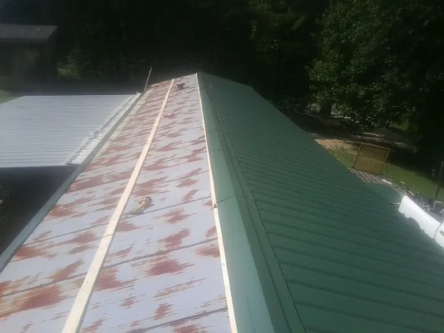 Old rusted panels beside newly installed green metal roofing — Wind Damage Roof Repair by Roofing Brothers in Guy