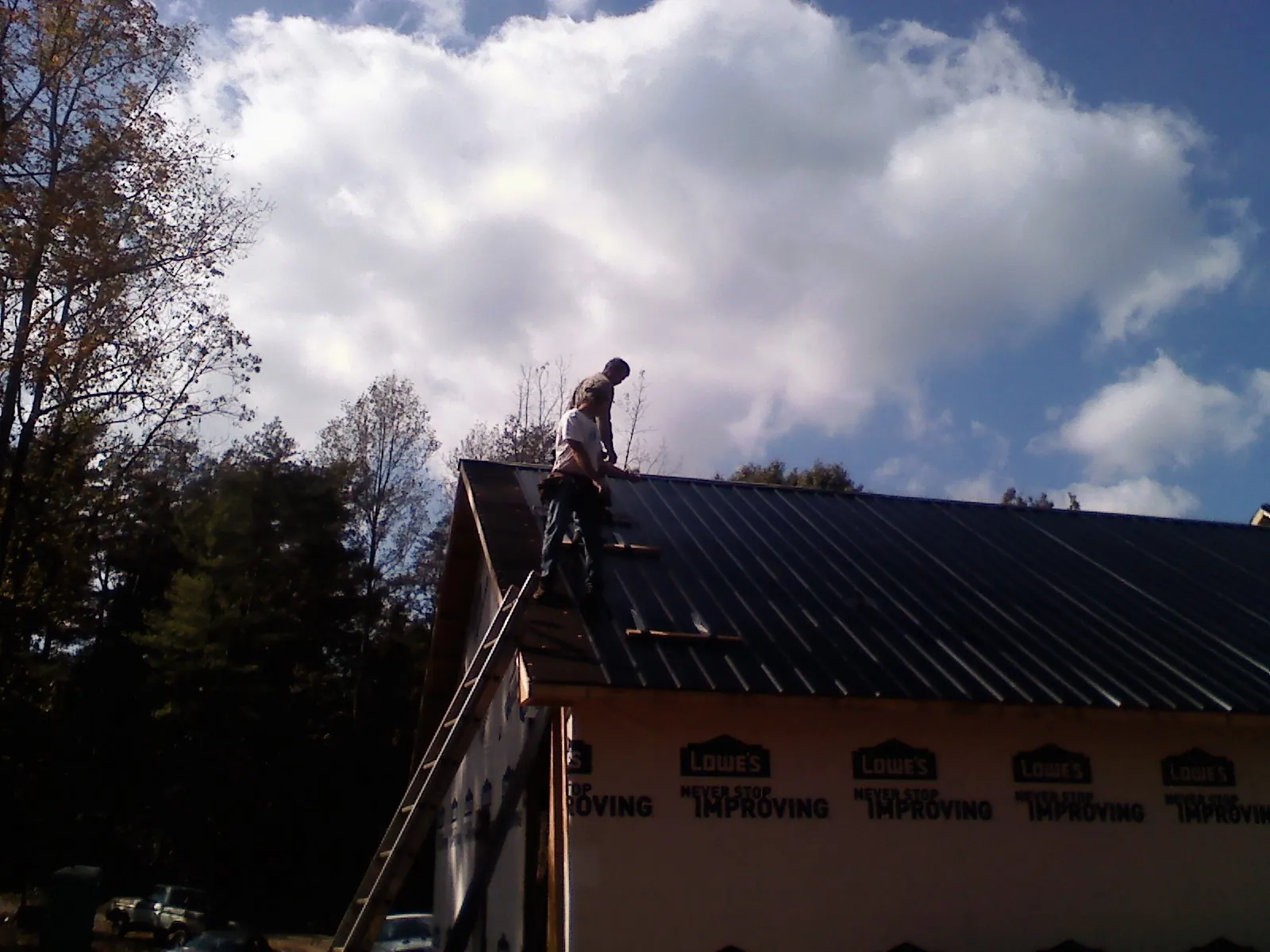 Roofer fastening dark metal panels high against a cloudy sky, from a Roof Inspection job in Guy