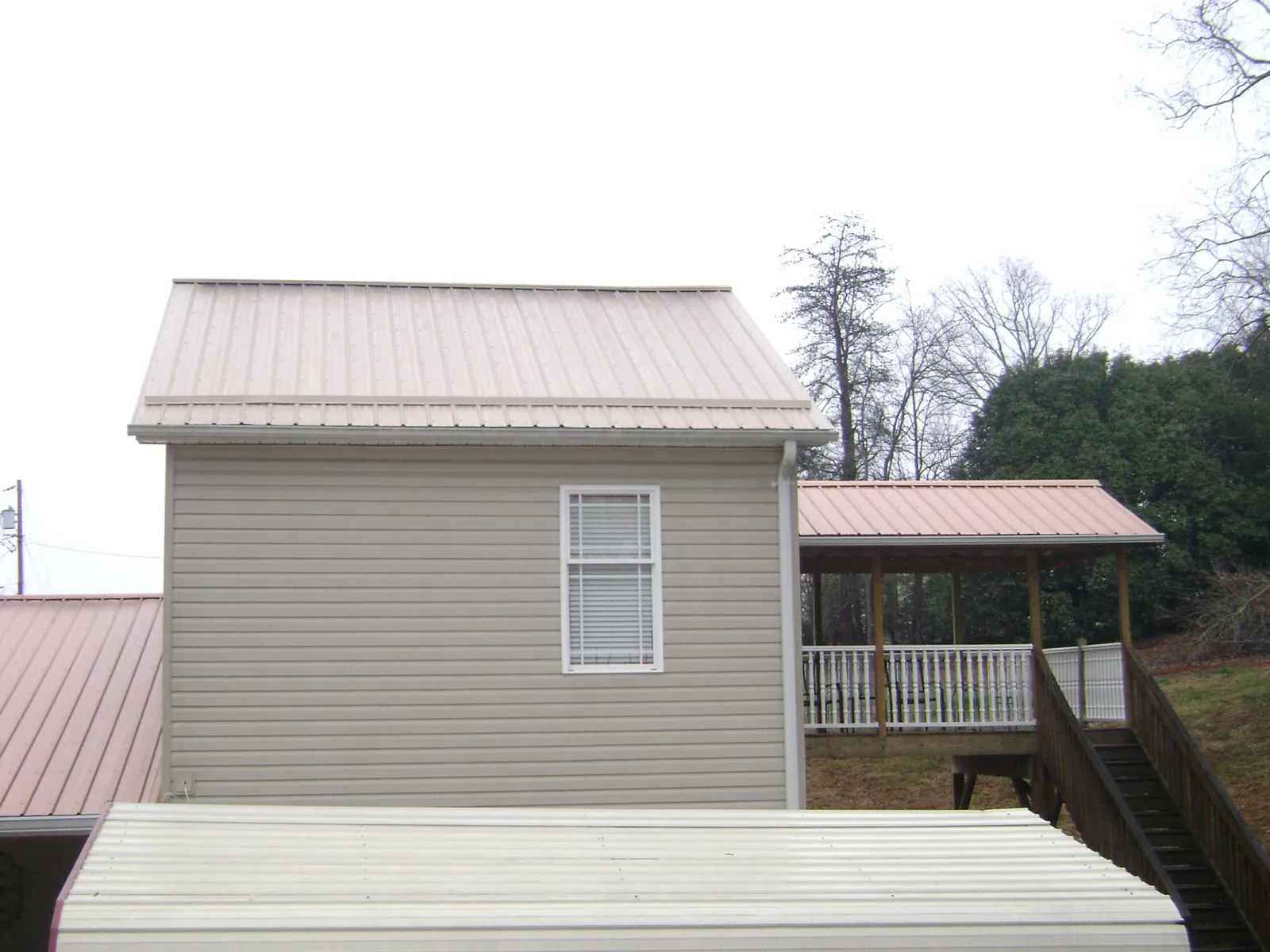 Tan metal roofs on a two story addition and attached porch, from a Roof Replacement job in Guy
